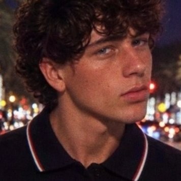 Close-up portrait of Miles Ketcham in a black polo, with blurred city lights behind him at night.